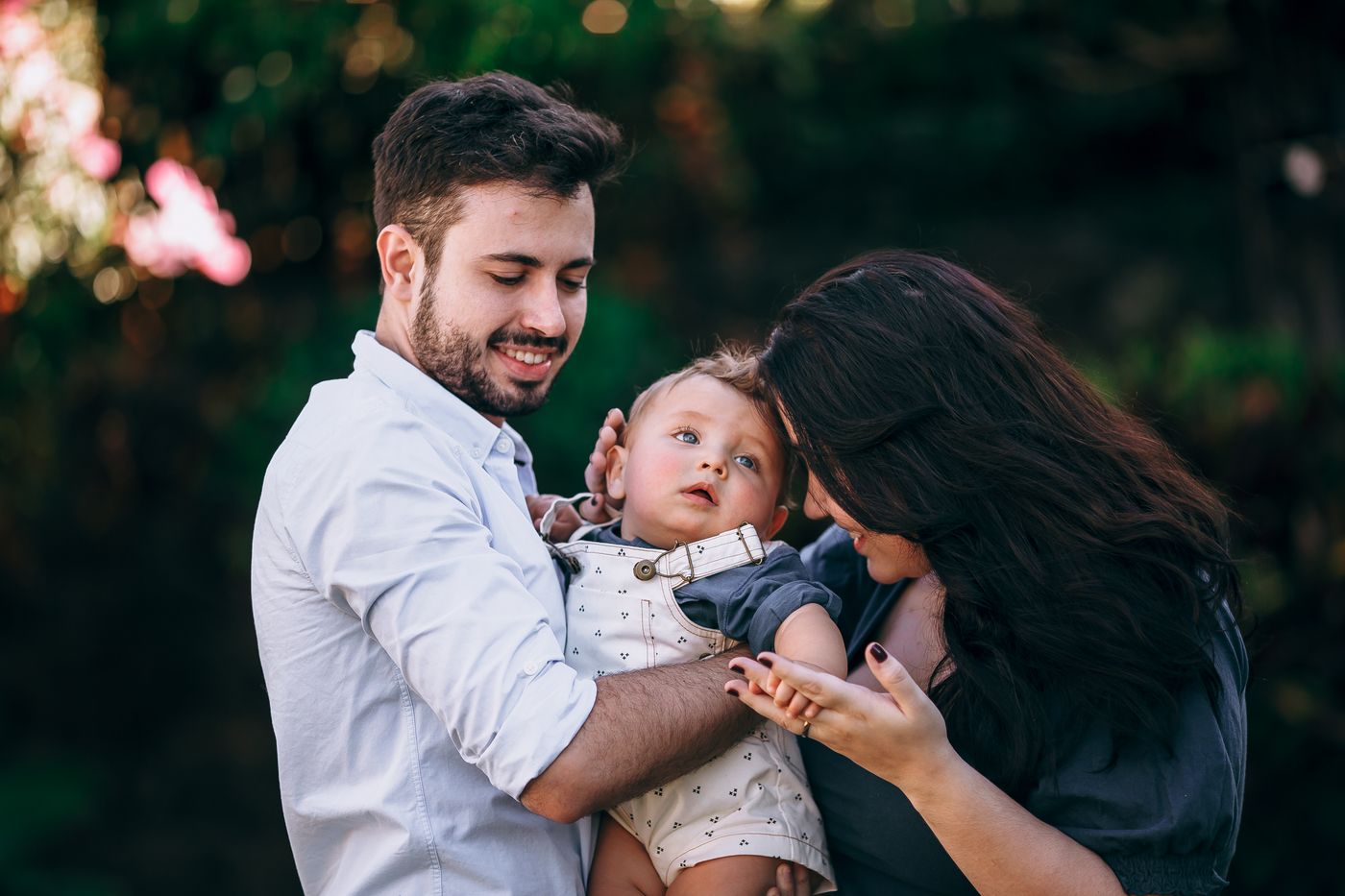 Casal sorrindo com o filho bebê no colo, ao ar livre